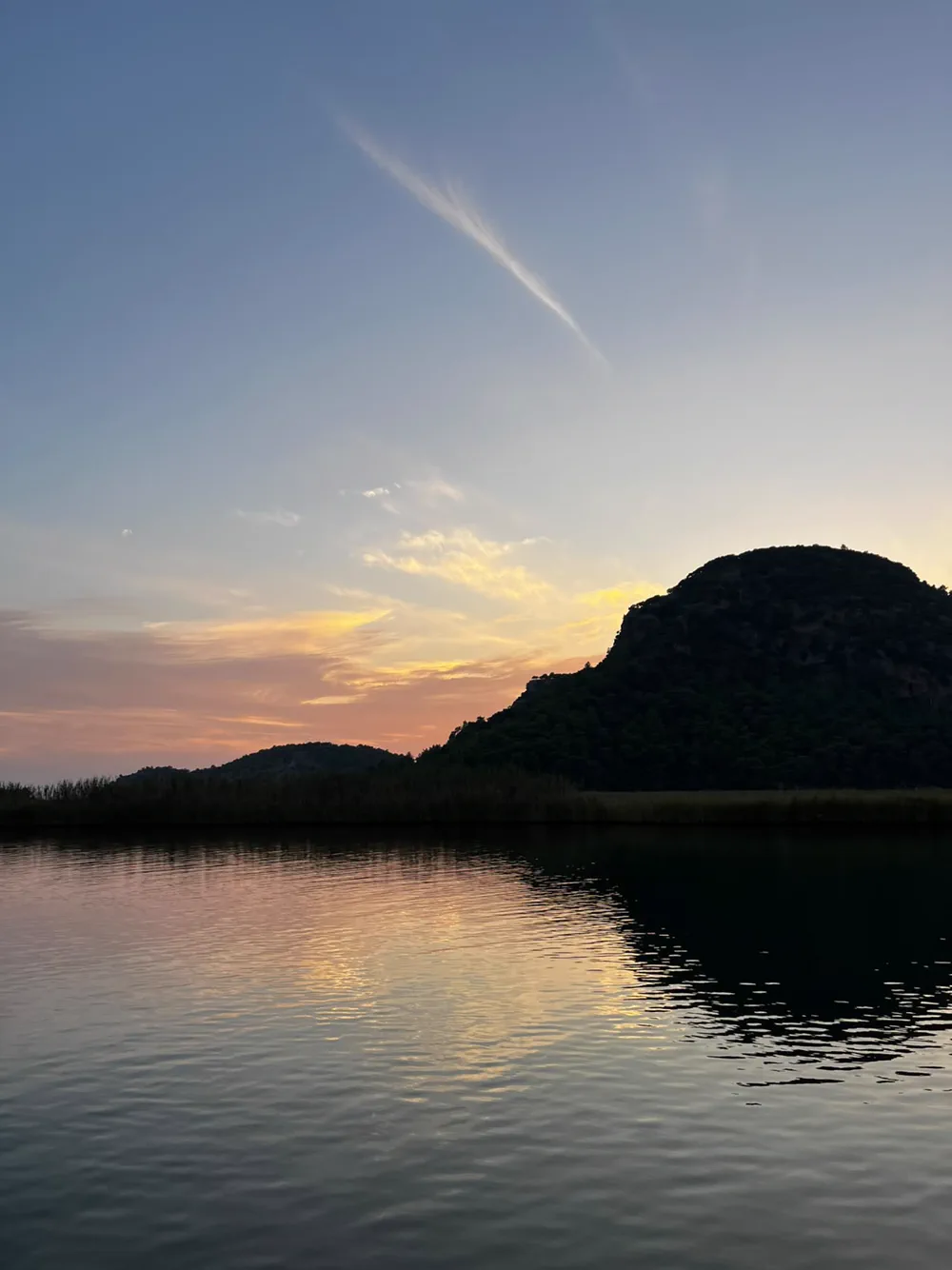 Dalyan’da gün batımı: karşıdaki tepenin silueti, altın rengine dönmüş su ve önde sazlık şeridi