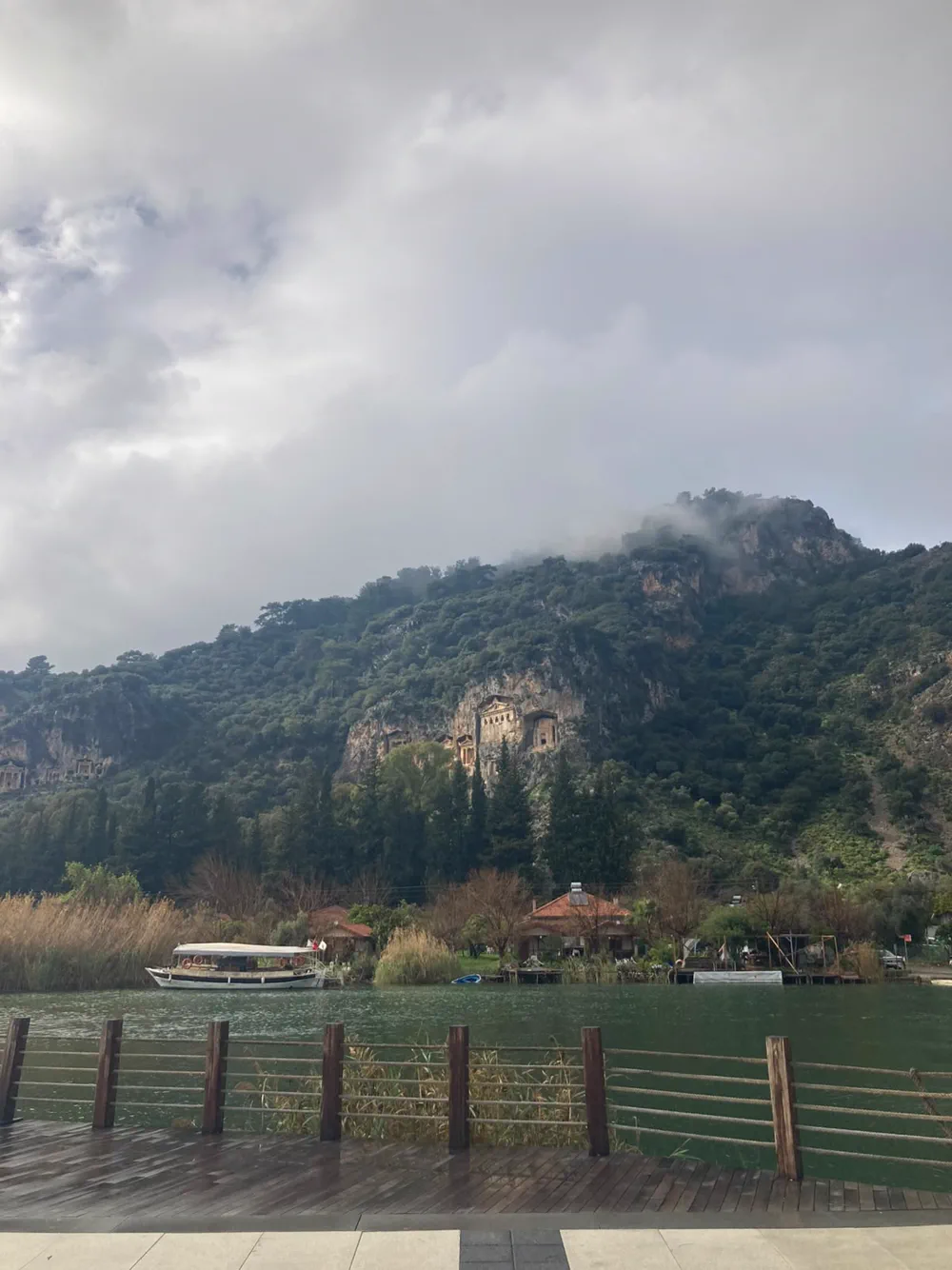 Bulutun yamaca indiği bir günde Dalyan kaya mezarları, altında bağlı bir tekne ve karşı kıyıdaki evler