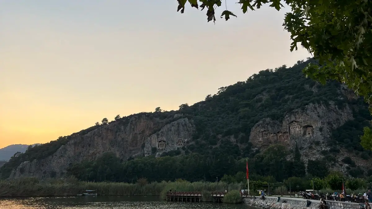 Gün batımında Kaunos kaya mezarları; kayalık batı ışığında bal rengine dönüyor, önünde Dalyan Çayı ve sazlıklar