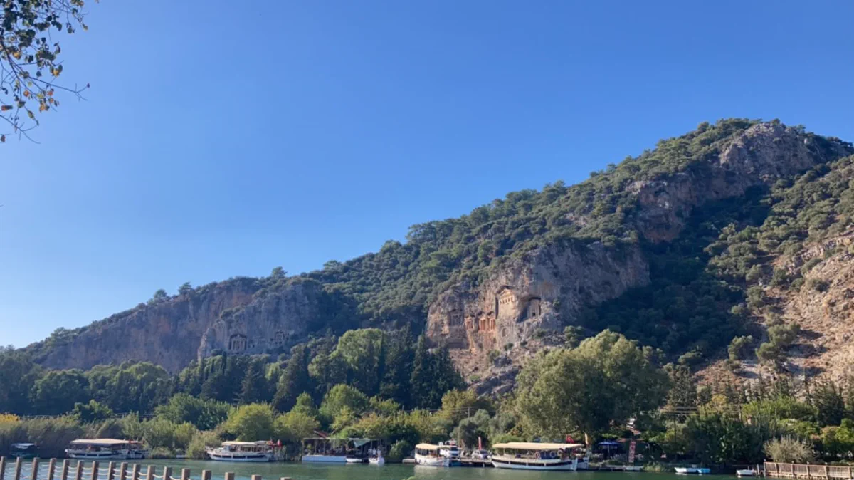 Dalyan Çayı’nın karşı kıyısındaki kayalıkta sıralanan Kaunos kaya mezarları ve kıyıdaki iskelelere bağlı tenteli tur tekneleri