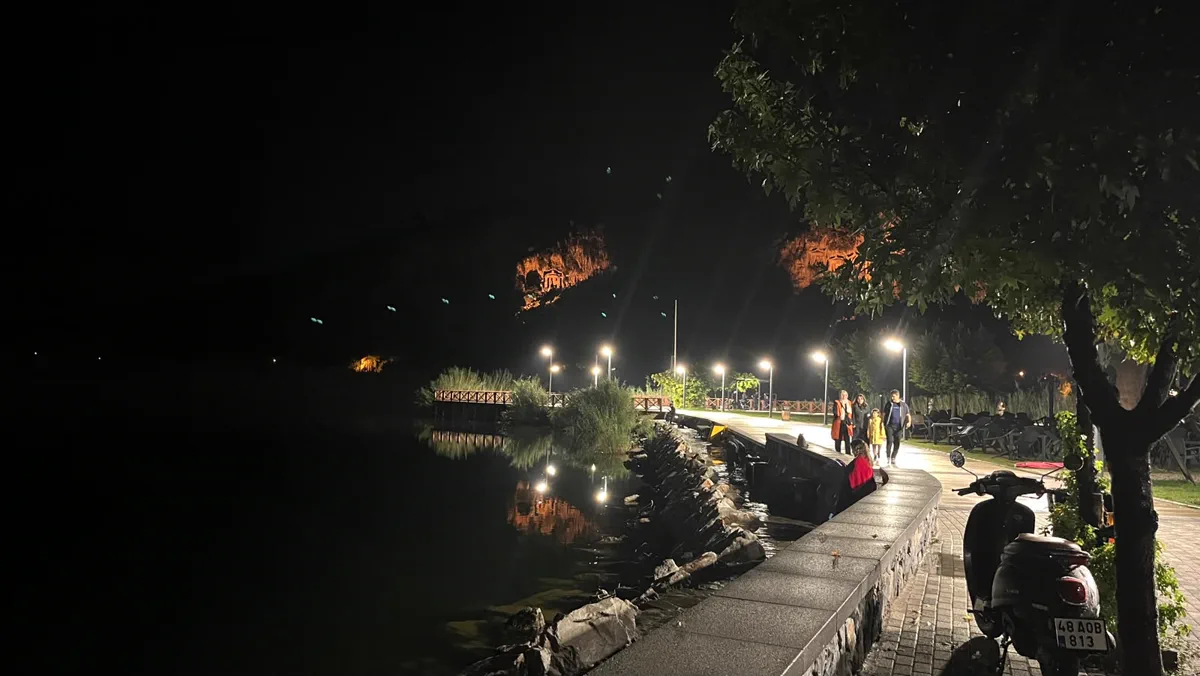 Gece kordon yürüyüş yolu, kıyıdaki taş duvar ve karşı yamaçta ışıklandırılmış kaya mezarları