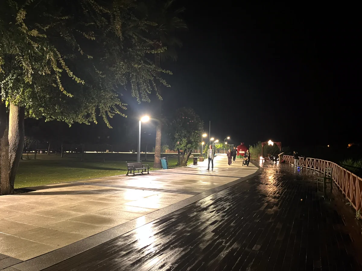 Gece Dalyan kordonu: ıslak ahşap yürüyüş yolu, sokak lambaları, banklar ve yürüyen aileler