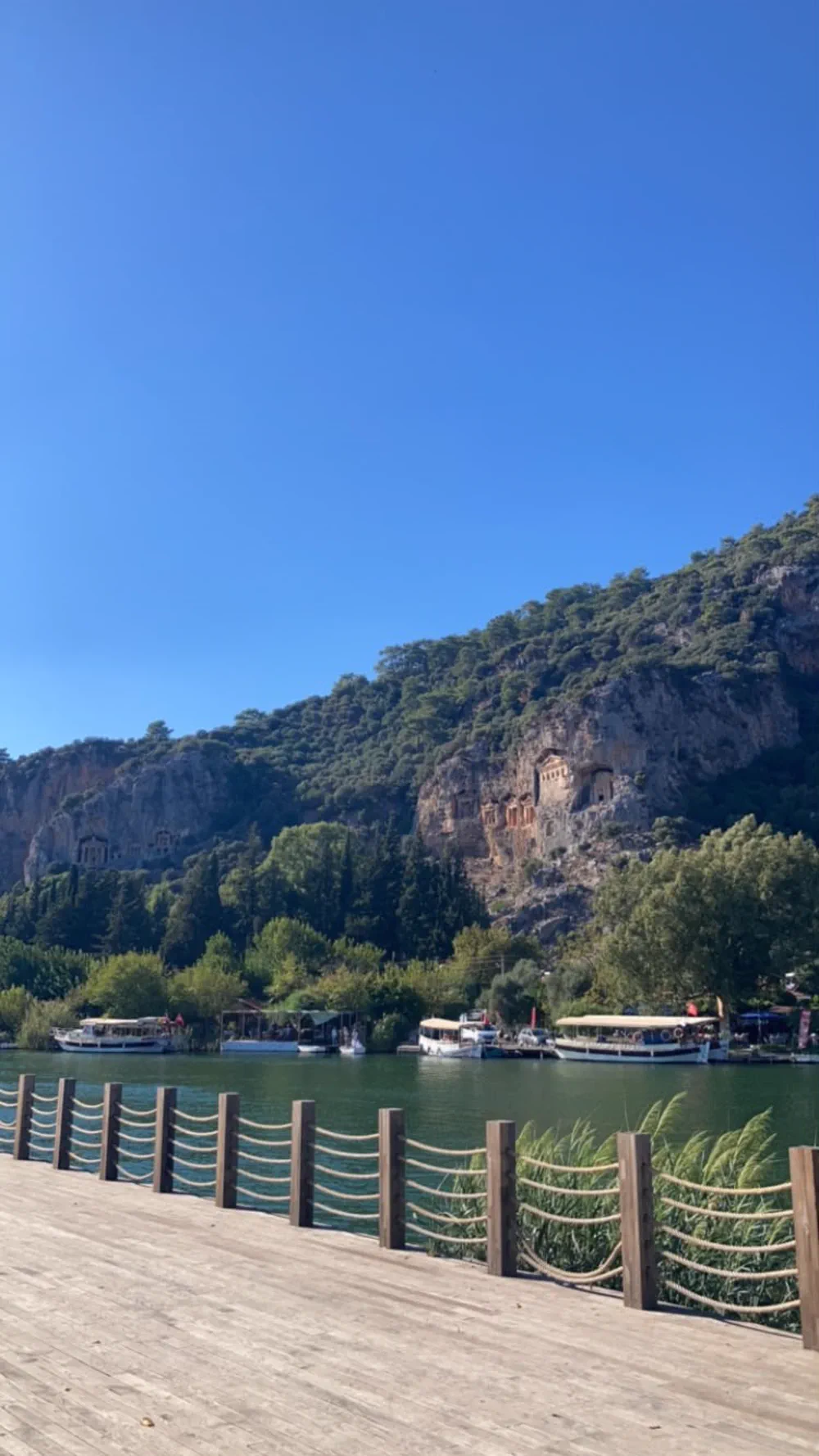 Dalyan kordonundaki ahşap yürüyüş yolunun halatlı korkuluğu ve karşı kayalıktaki kral mezarları