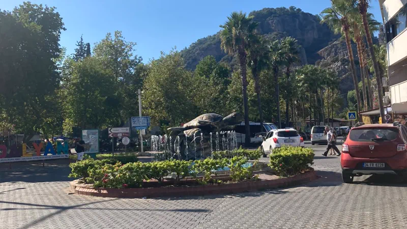 Dalyan meydanı: caretta heykelli havuz, palmiyeler ve arkada kayalık tepe