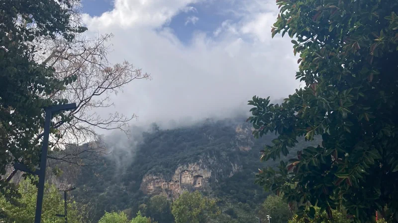 Dalyan’da taş döşeli park alanı ve arkada bulutun indiği yamaçta kaya mezarları