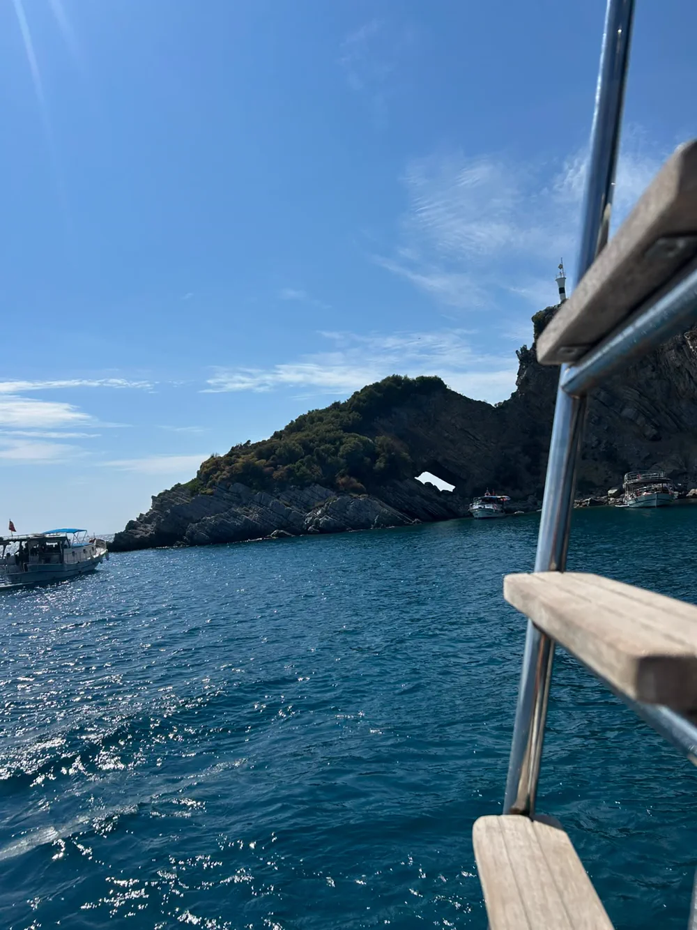 Teknenin küpeştesinden kayalık bir burun, kayadaki delik ve koya demirlemiş tur tekneleri